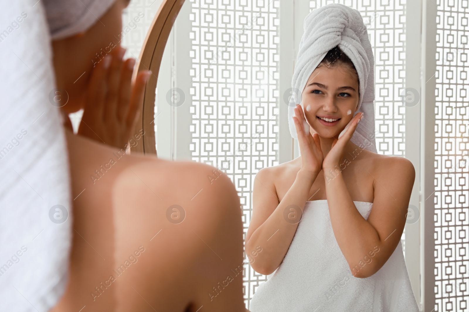 Photo of Beautiful teenage girl applying cleansing foam onto face near mirror at home. Skin care cosmetic