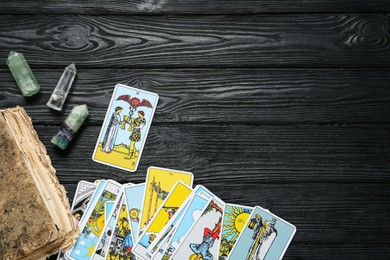 Tarot cards, old book and crystals on black wooden table, flat lay. Space for text