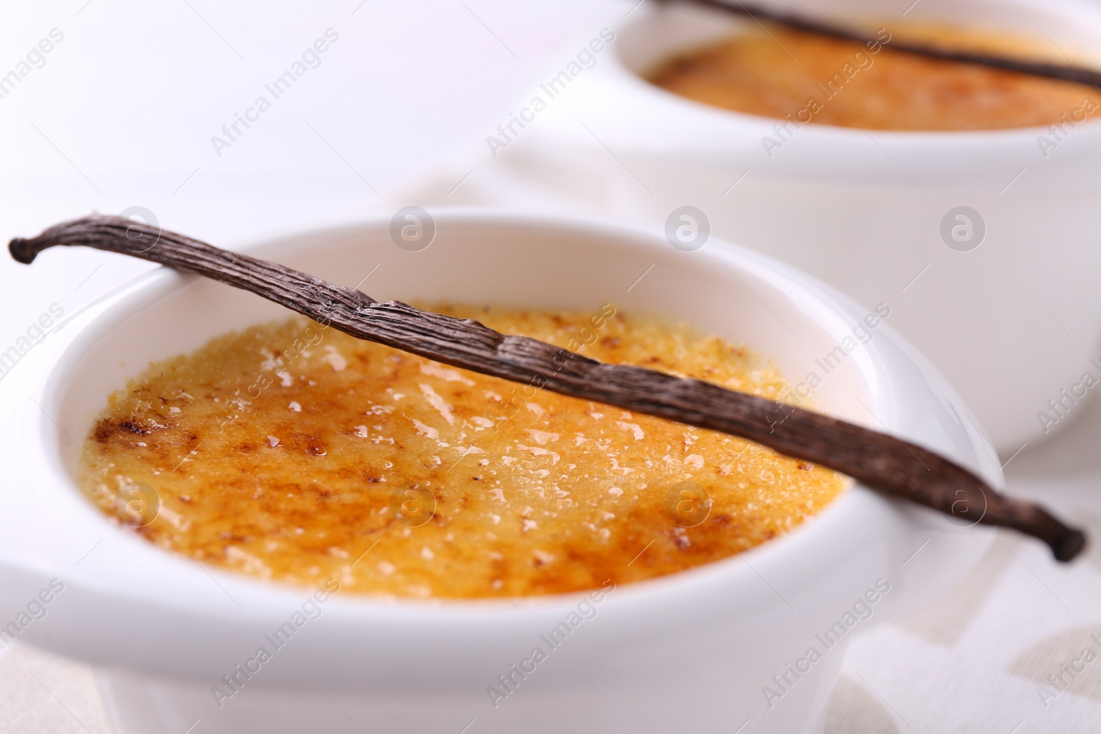 Photo of Delicious creme brulee in bowl and vanilla pod on table, closeup