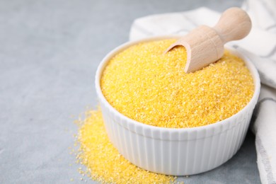 Raw cornmeal and scoop in bowl on grey table, closeup. Space for text