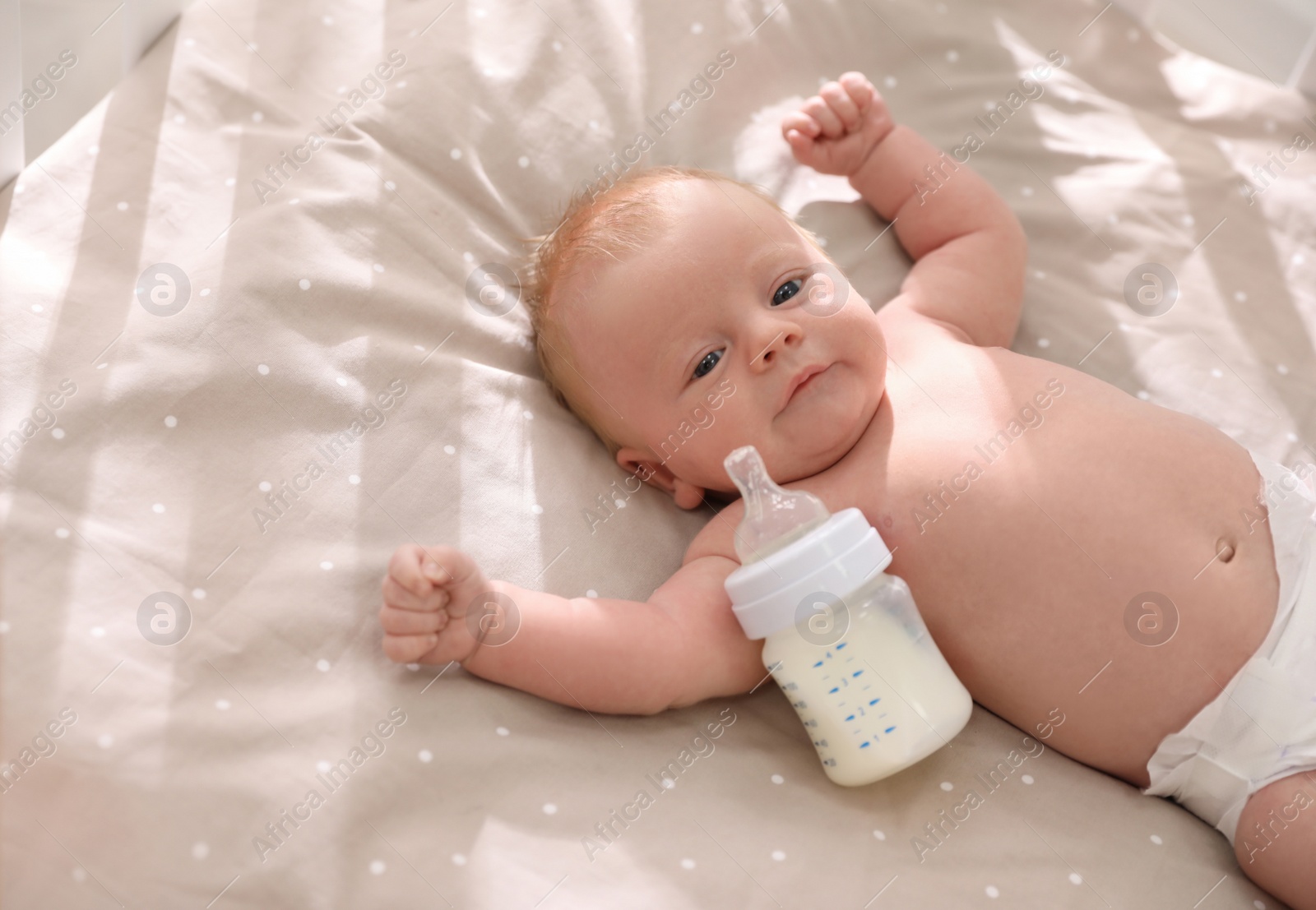 Photo of Cute healthy baby with bottle of milk lying in cot