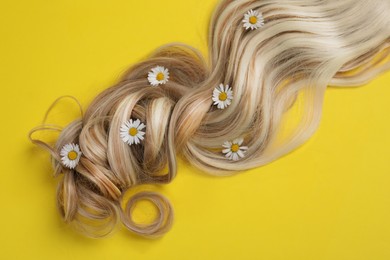 Photo of Lock of healthy blond hair with flowers on yellow background, top view