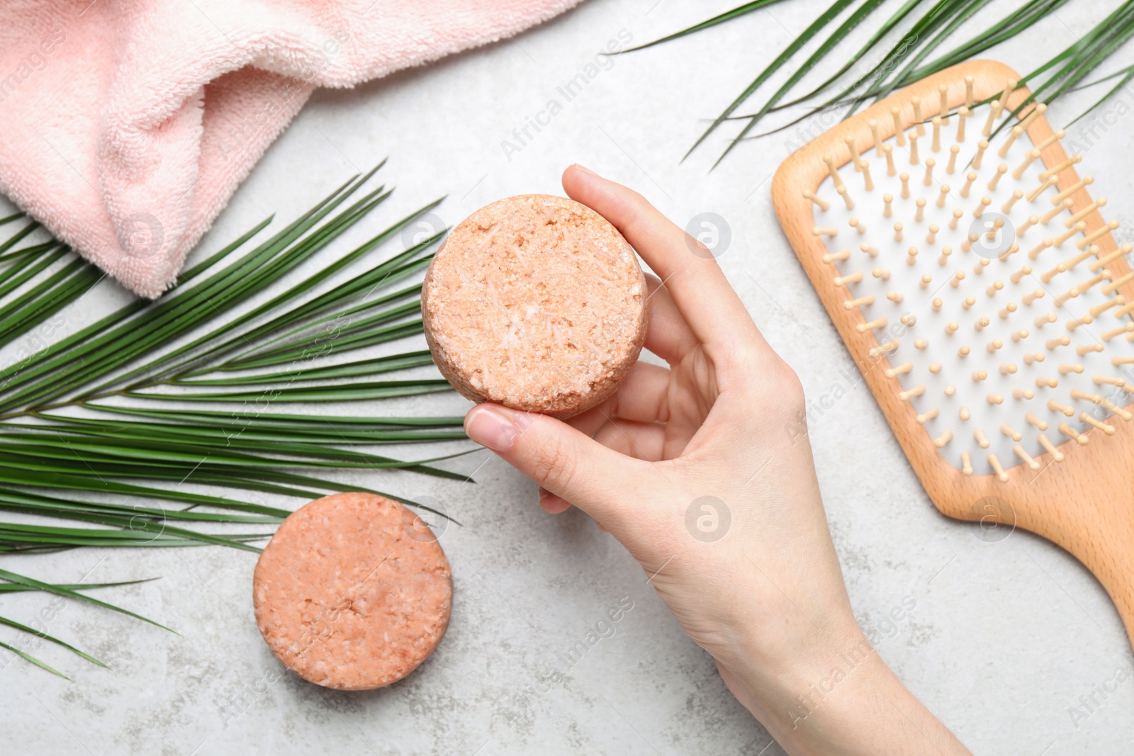 Photo of Woman holding solid shampoo bar at light grey table, top view. Hair care