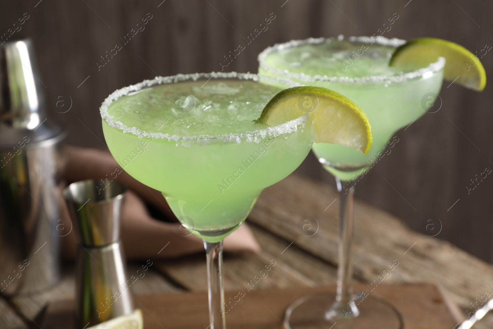 Photo of Delicious Margarita cocktail with ice cubes in glasses and lime on wooden table, closeup