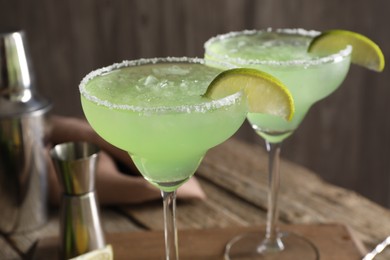 Delicious Margarita cocktail with ice cubes in glasses and lime on wooden table, closeup