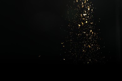 Photo of Shiny golden glitter falling down on black background. Bokeh effect