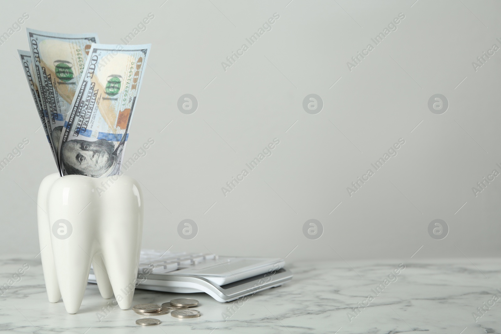 Photo of Ceramic model of tooth, money and calculator on white marble table, space for text. Expensive treatment