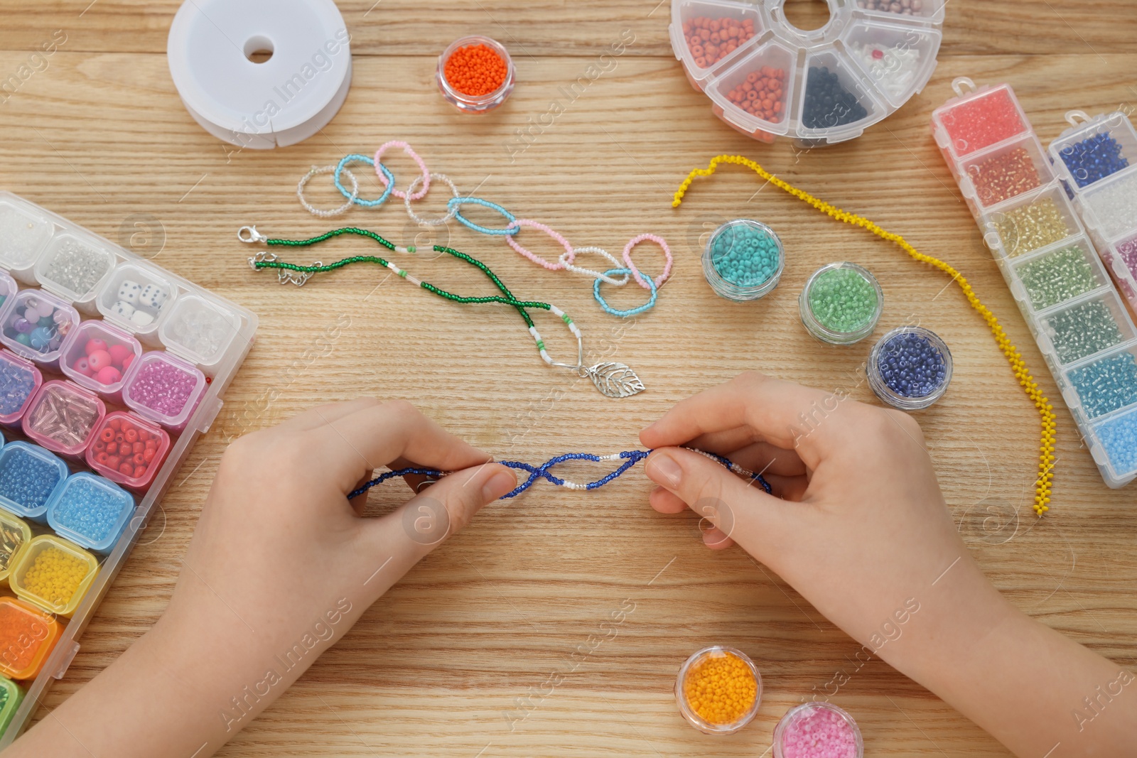 Photo of Girl making beaded jewelry at wooden table, top view