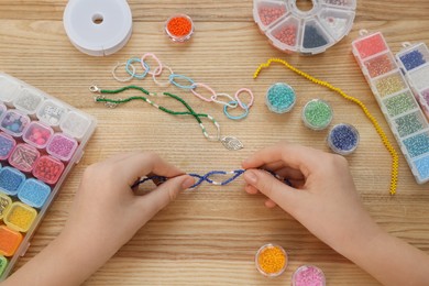 Girl making beaded jewelry at wooden table, top view