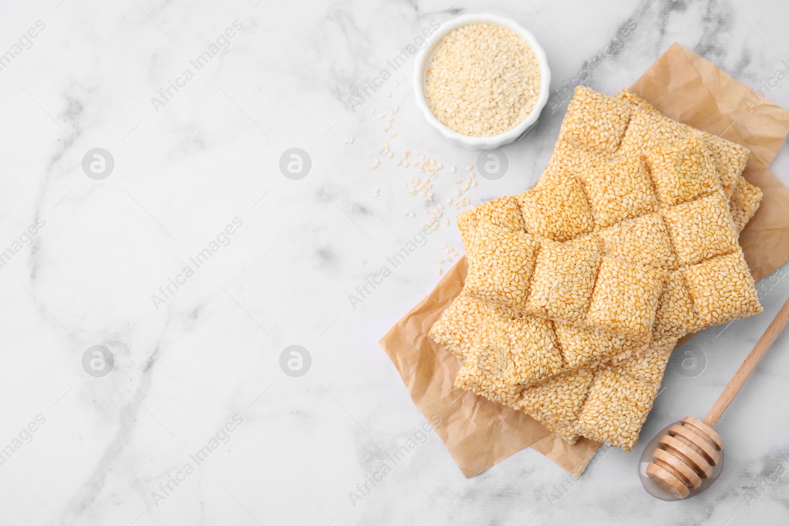 Photo of Delicious sweet kozinaki bars, sesame seeds and wooden dipper on white marble table, flat lay. Space for text