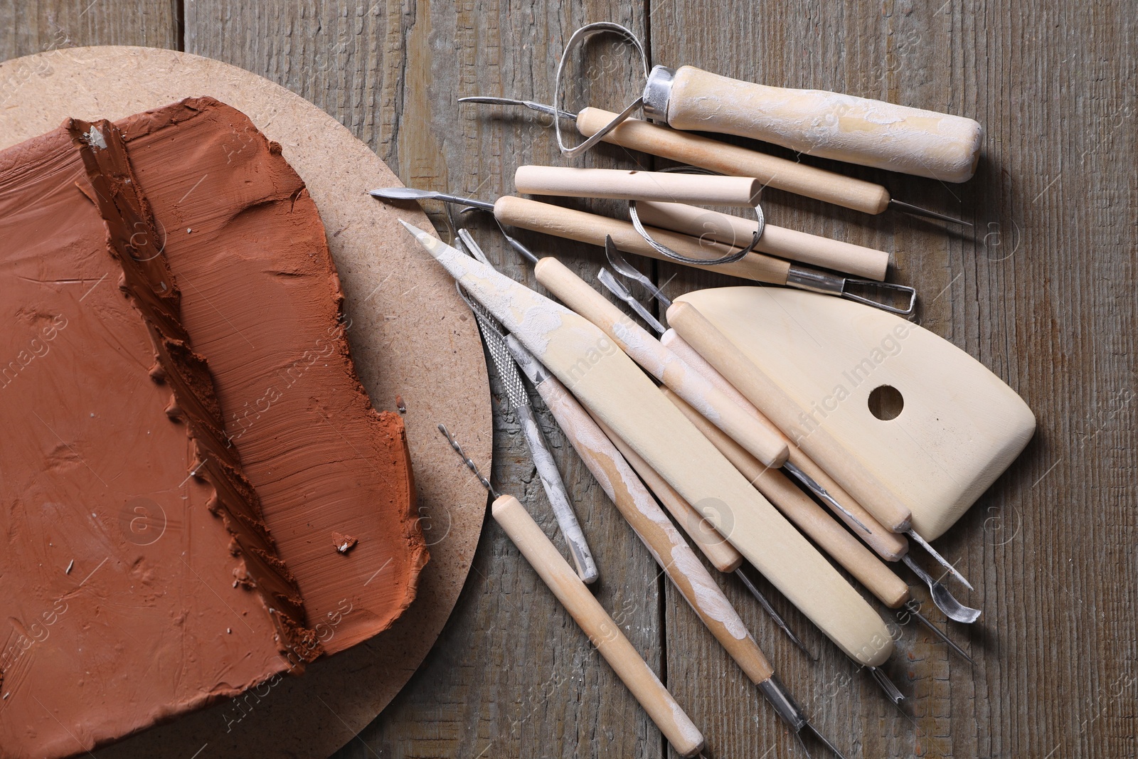 Photo of Clay and set of modeling tools on wooden table, flat lay