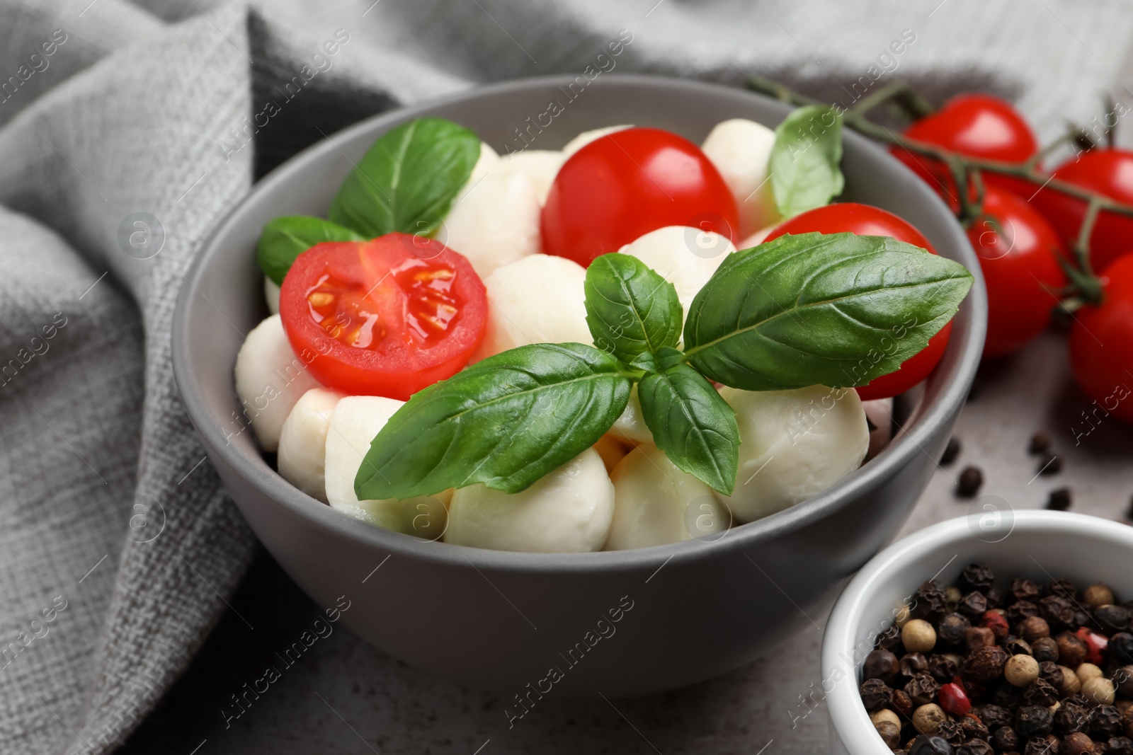 Photo of Delicious mozzarella balls in bowl, tomatoes and basil leaves on table, closeup