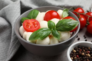 Delicious mozzarella balls in bowl, tomatoes and basil leaves on table, closeup