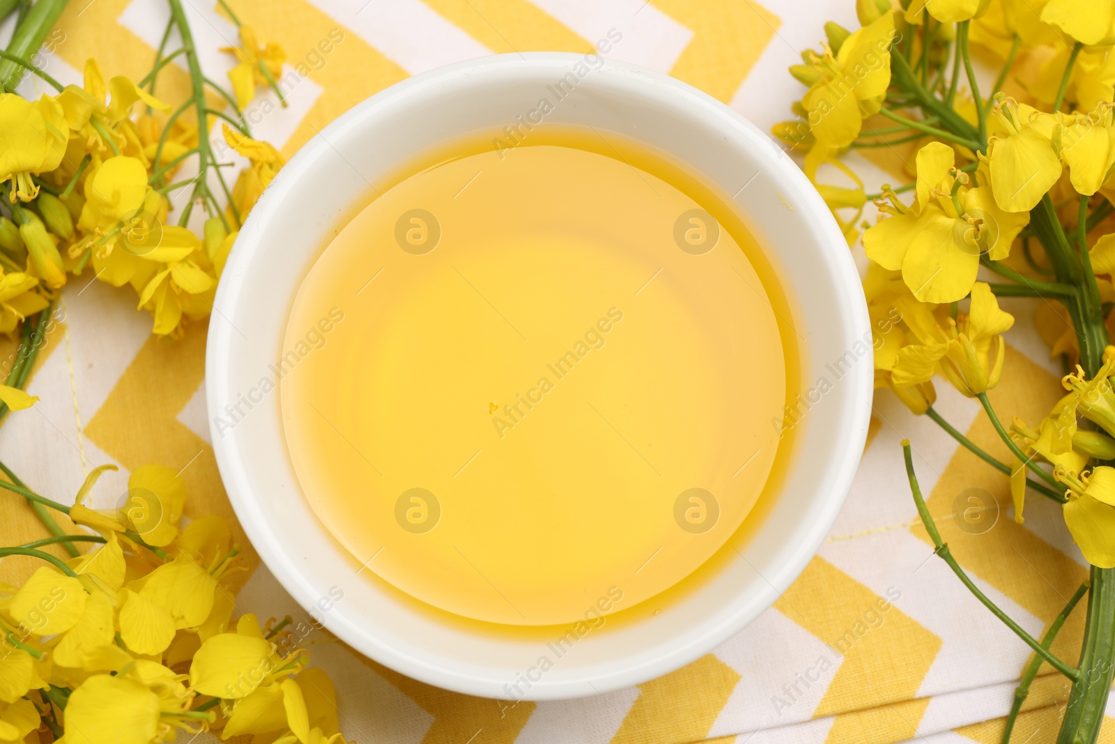 Photo of Rapeseed oil in bowl and beautiful yellow flowers on table, top view
