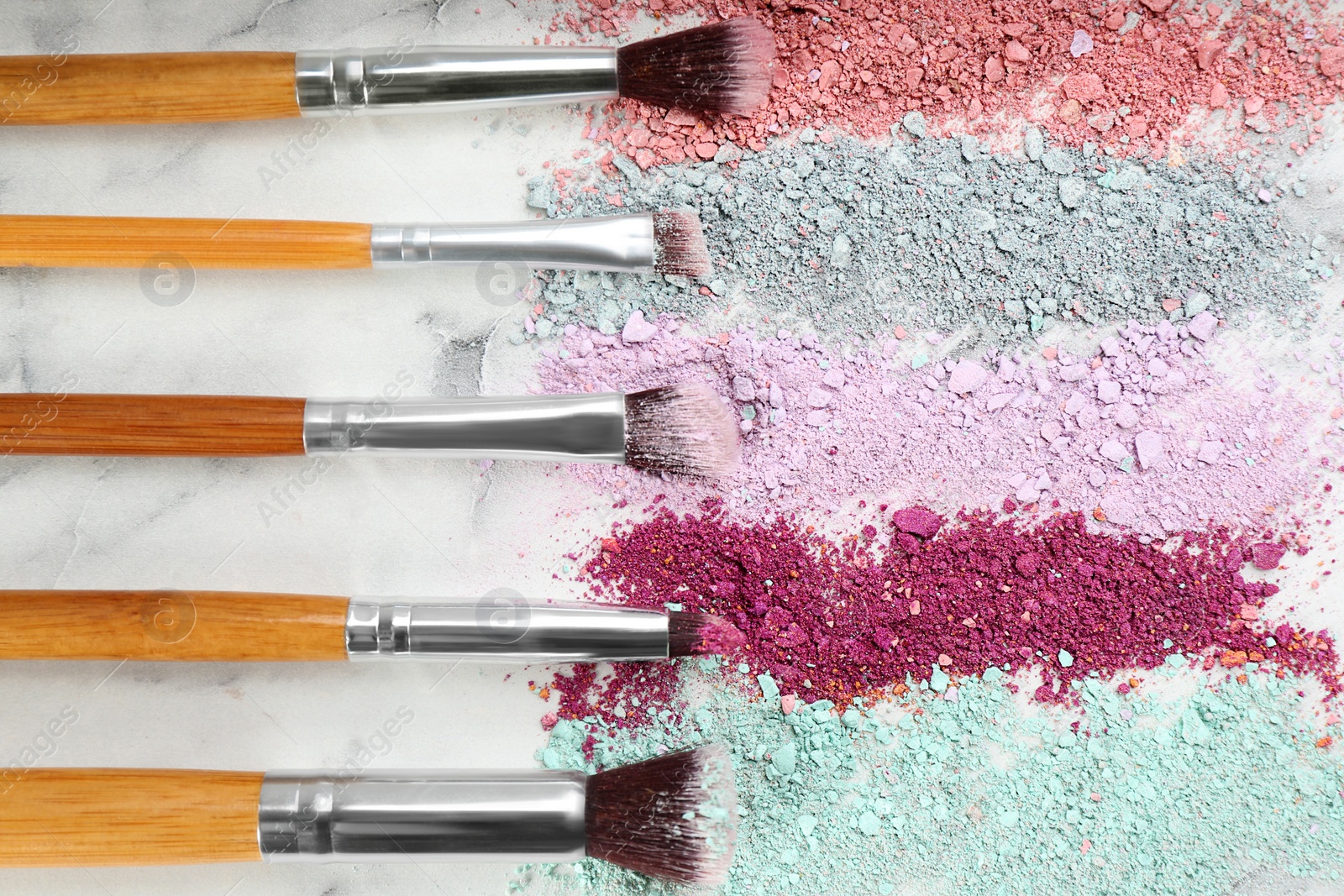 Photo of Makeup brushes and scattered eye shadows on white marble table, flat lay