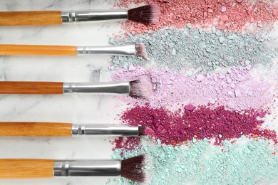 Makeup brushes and scattered eye shadows on white marble table, flat lay