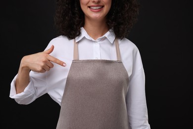 Photo of Woman pointing at kitchen apron on black background, closeup. Mockup for design