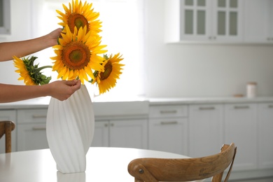 Photo of Woman making bouquet of sunflowers in kitchen, closeup. Space for text