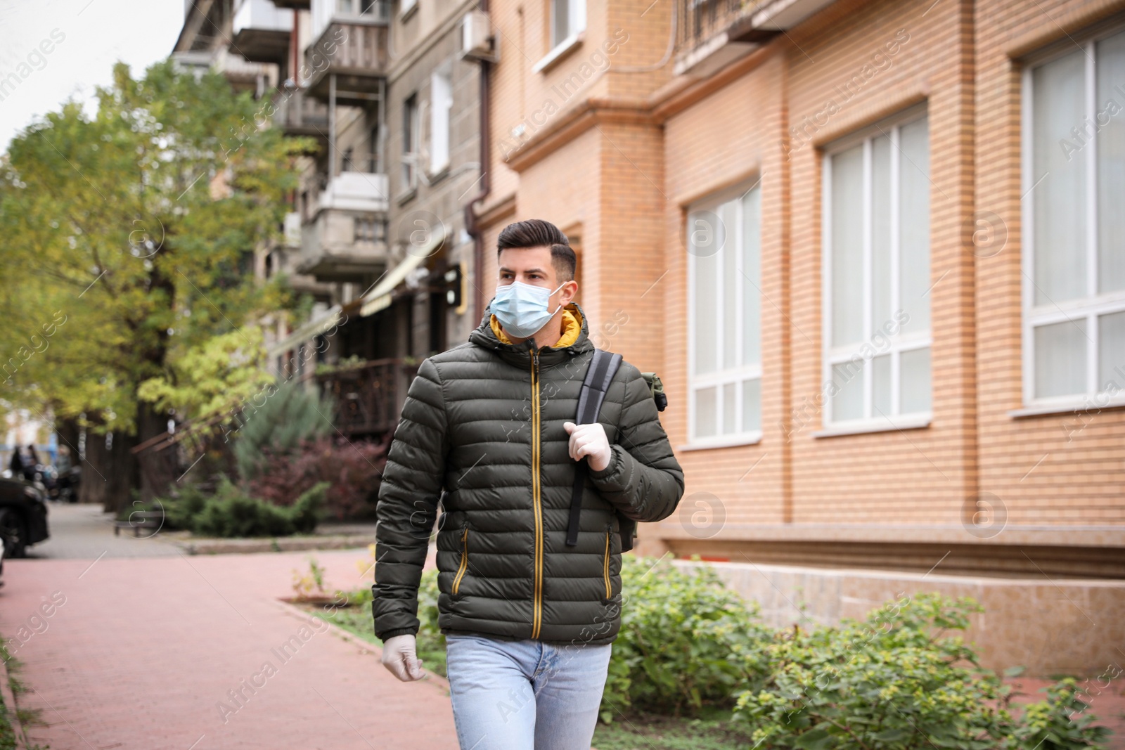 Photo of Man in medical face mask and gloves walking outdoors. Personal protection during COVID-19 pandemic