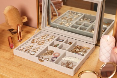 Photo of Elegant jewelry box with beautiful bijouterie, burning candles and makeup products on wooden table