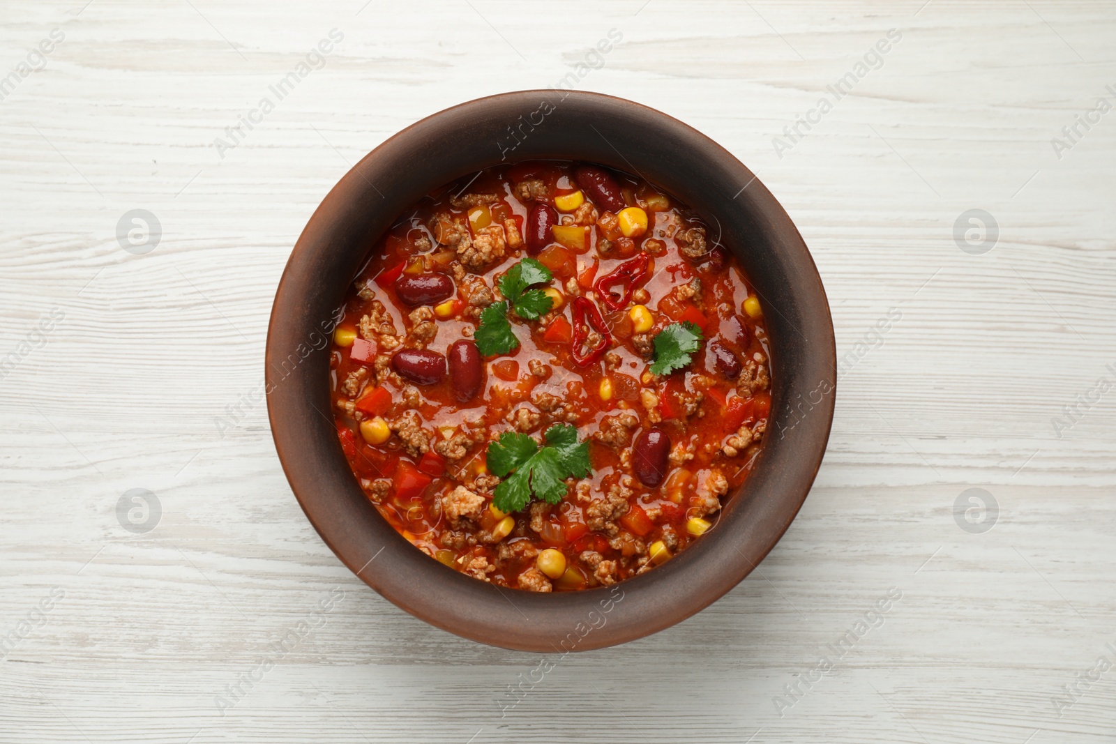 Photo of Bowl with tasty chili con carne on white wooden table, top view