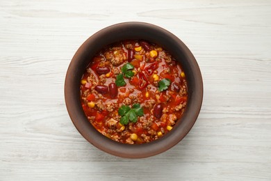 Bowl with tasty chili con carne on white wooden table, top view