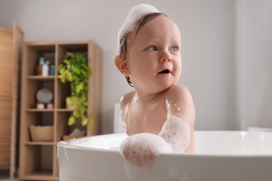 Photo of Cute little baby taking foamy bath at home