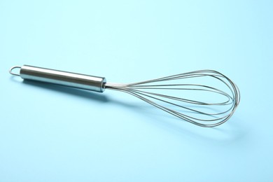 Photo of One metal whisk on light blue background