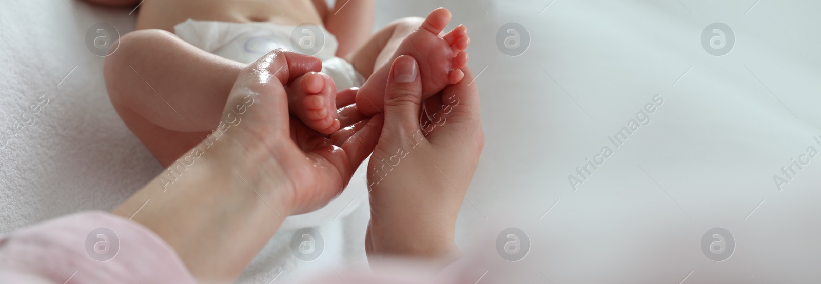 Image of Mother massaging her cute baby with oil on changing table, closeup. Banner design with space for text