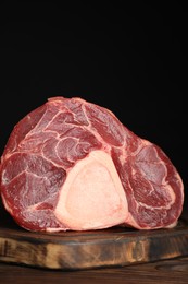 Photo of Piece of raw beef meat on wooden table against black background, closeup