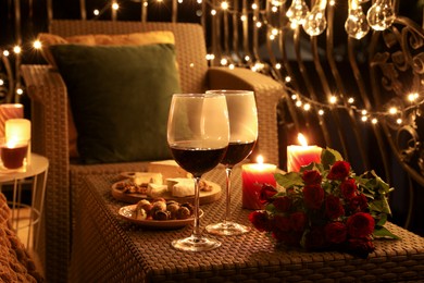 Bouquet of roses, glasses with wine, snacks and candles on rattan table at balcony in night