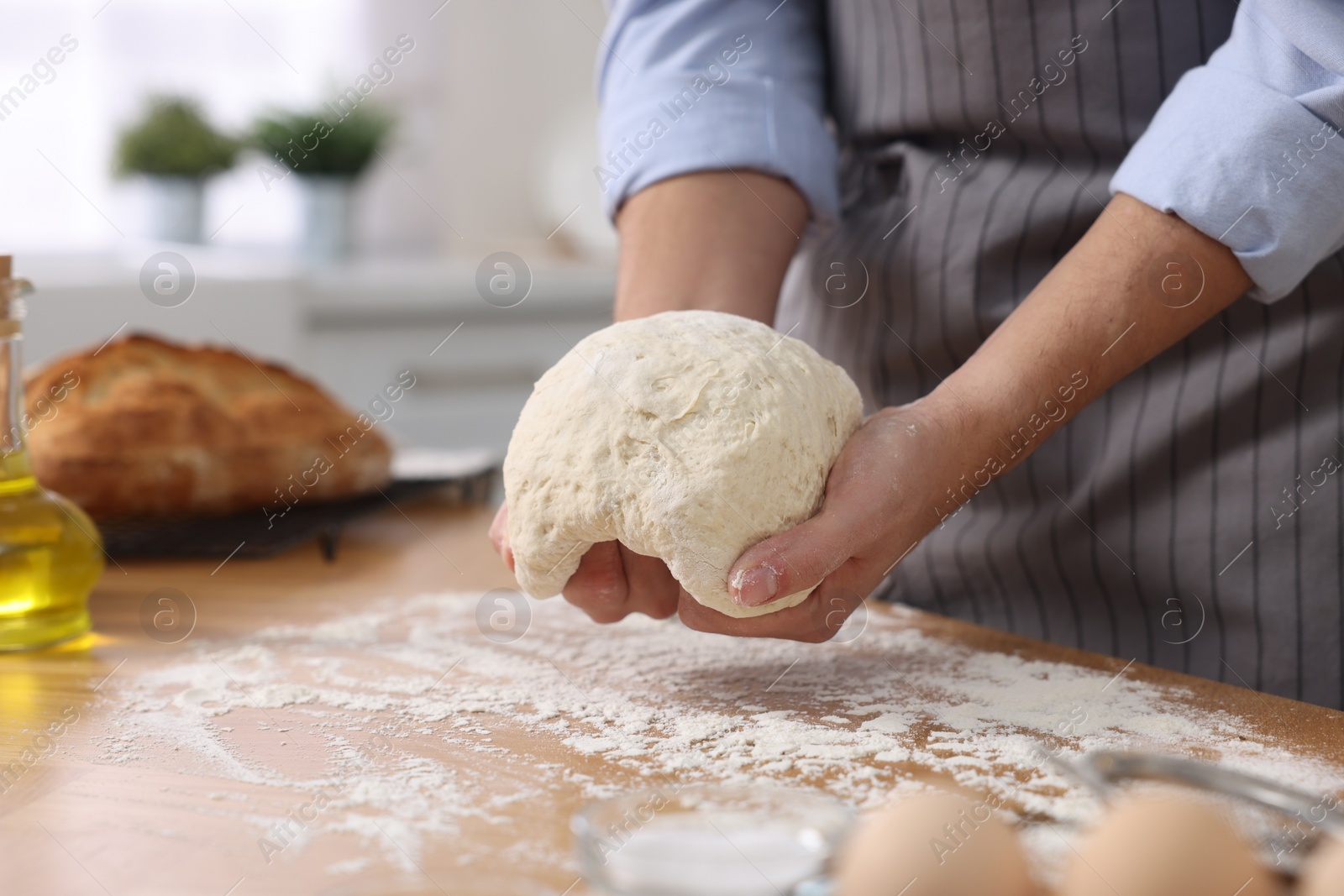 Photo of Making bread. Man kneading dough at wooden table in kitchen, closeup