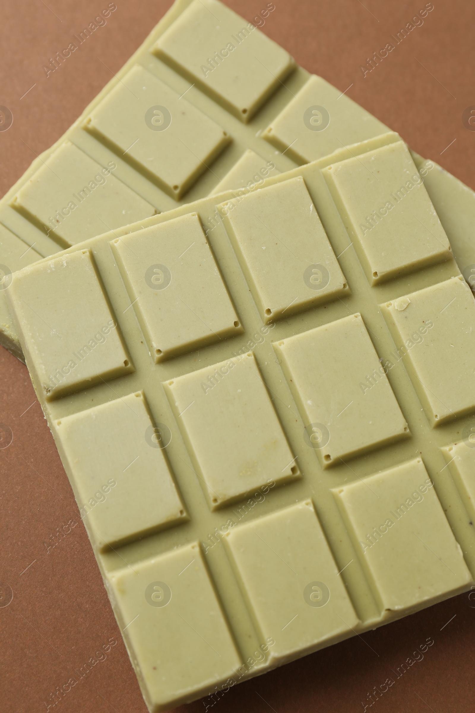 Photo of Pieces of tasty matcha chocolate bar on brown background, closeup