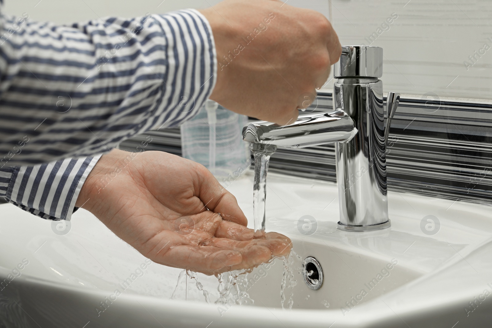 Photo of Man using water tap to wash hands in bathroom, closeup