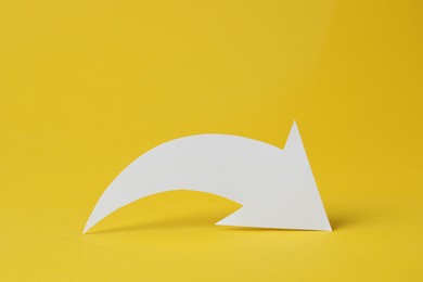 Photo of White curved paper arrow on yellow background