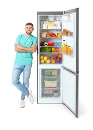 Young man near open refrigerator on white background