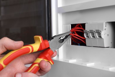 Professional repairman fixing electric panel with pliers indoors, closeup