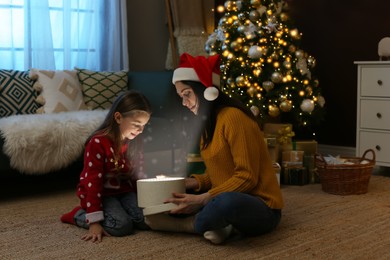 Mother with her cute daughter opening gift box at home. Christmas celebration