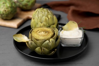Delicious cooked artichokes with tasty sauce served on grey wooden table, closeup