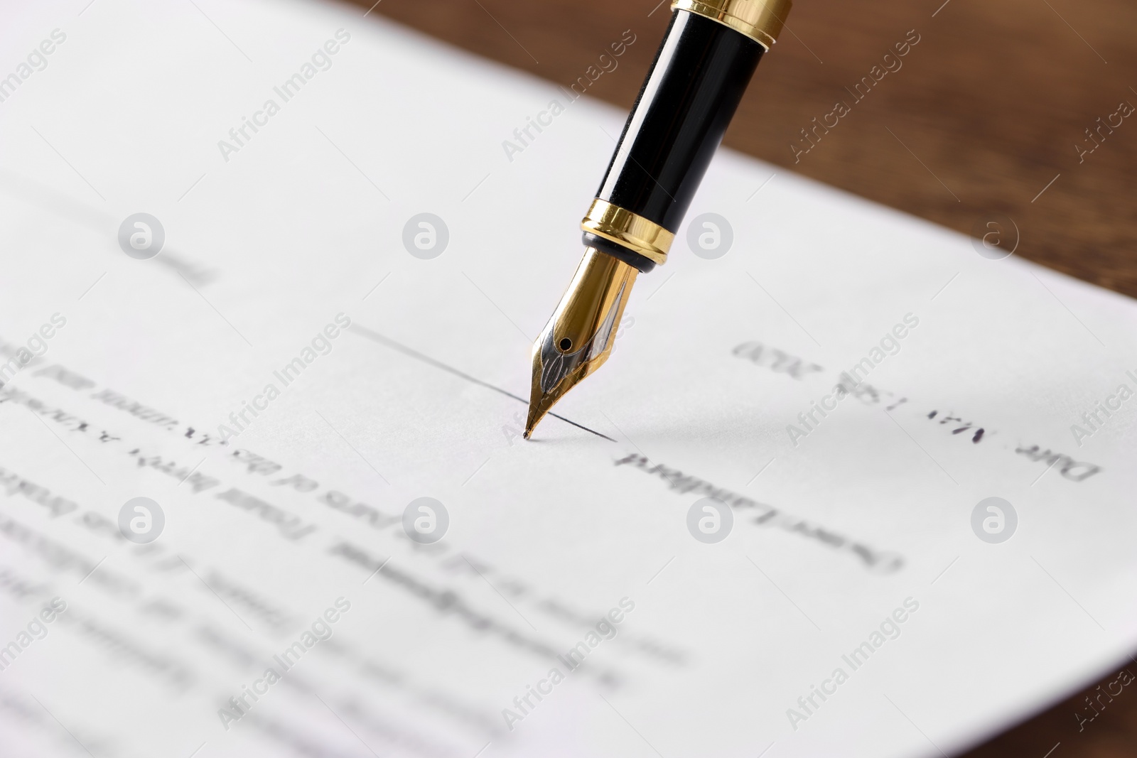 Photo of Writing on document with fountain pen at wooden table, closeup. Notary contract