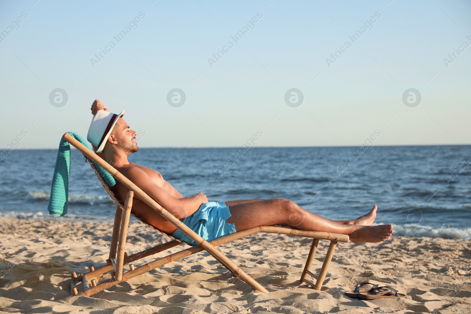 Photo of Young man relaxing in deck chair on beach near sea