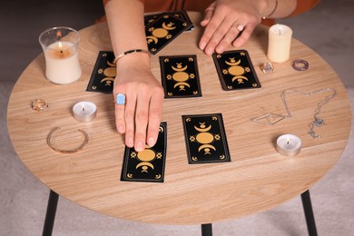 Photo of Soothsayer predicting future with tarot cards at table indoors, closeup