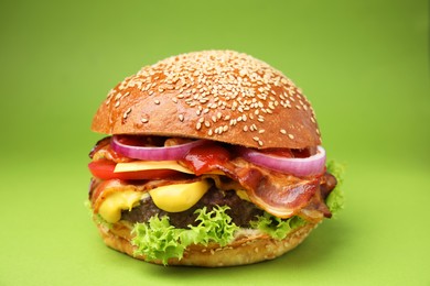 Delicious burger with bacon, patty and vegetables on green background, closeup