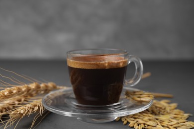 Photo of Cup of barley coffee, grains and spikes on gray table, closeup