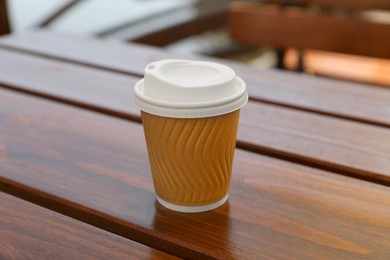 Takeaway paper cup with coffee on wooden table, closeup