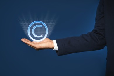 Image of Man holding virtual icon of copyright symbol on blue background, closeup