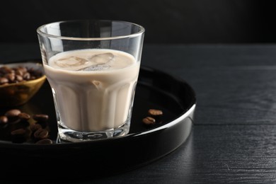 Photo of Coffee cream liqueur in glass and beans on black wooden table, space for text