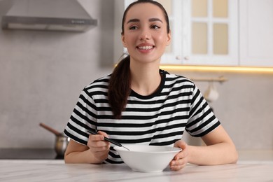 Woman eating tasty soup at white table in kitchen