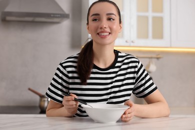 Photo of Woman eating tasty soup at white table in kitchen