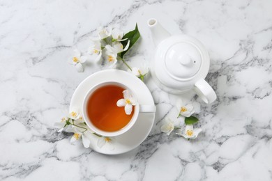 Photo of Aromatic jasmine tea and fresh flowers on white marble table, flat lay